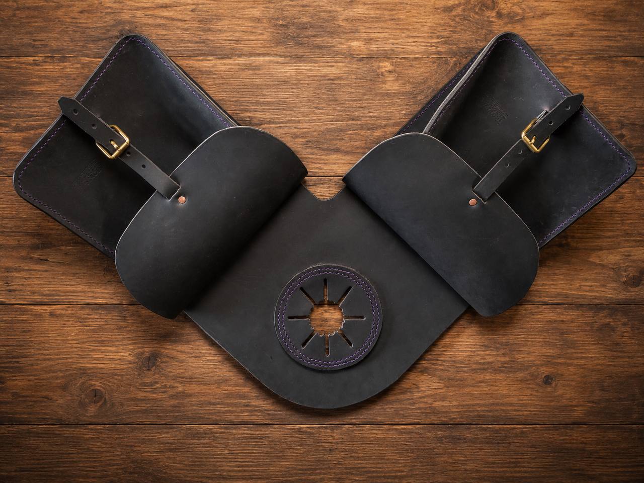 Black leather saddle bag set on a wood table.