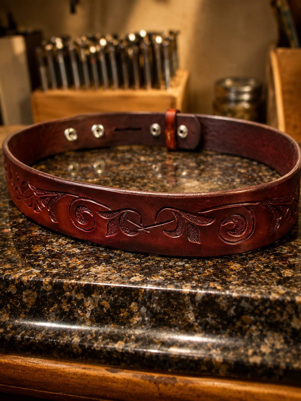 Brown floral tooled leather belt on a workbench.