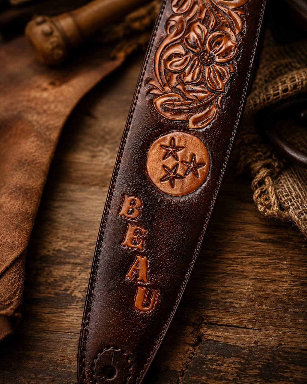 Close-up of a dark tooled leather guitar strap with floral carving and lettering.
