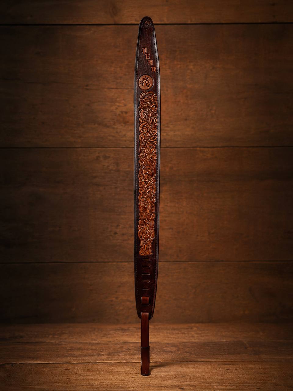 Full length dark tooled leather guitar strap on a warm wood background.