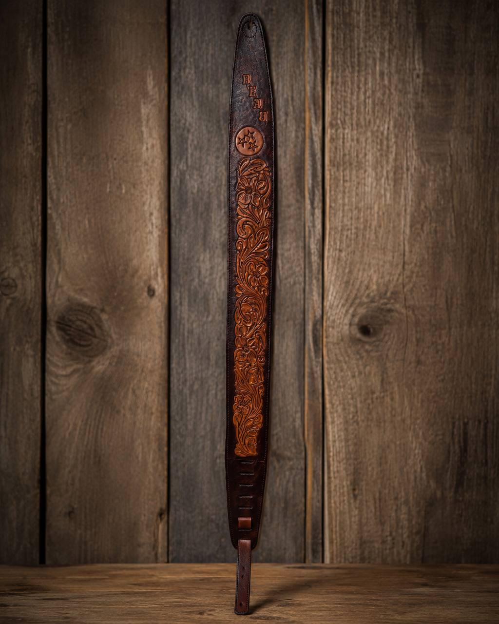 Full length dark tooled leather guitar strap on a wood plank background.